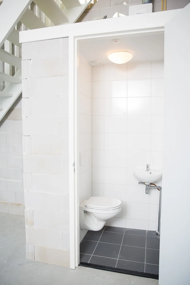 Kleine, witte toiletruimte met wandcloset en fonteintje onder een trap in een nieuwbouwwoning aan de Laan van S-Gravenmade.